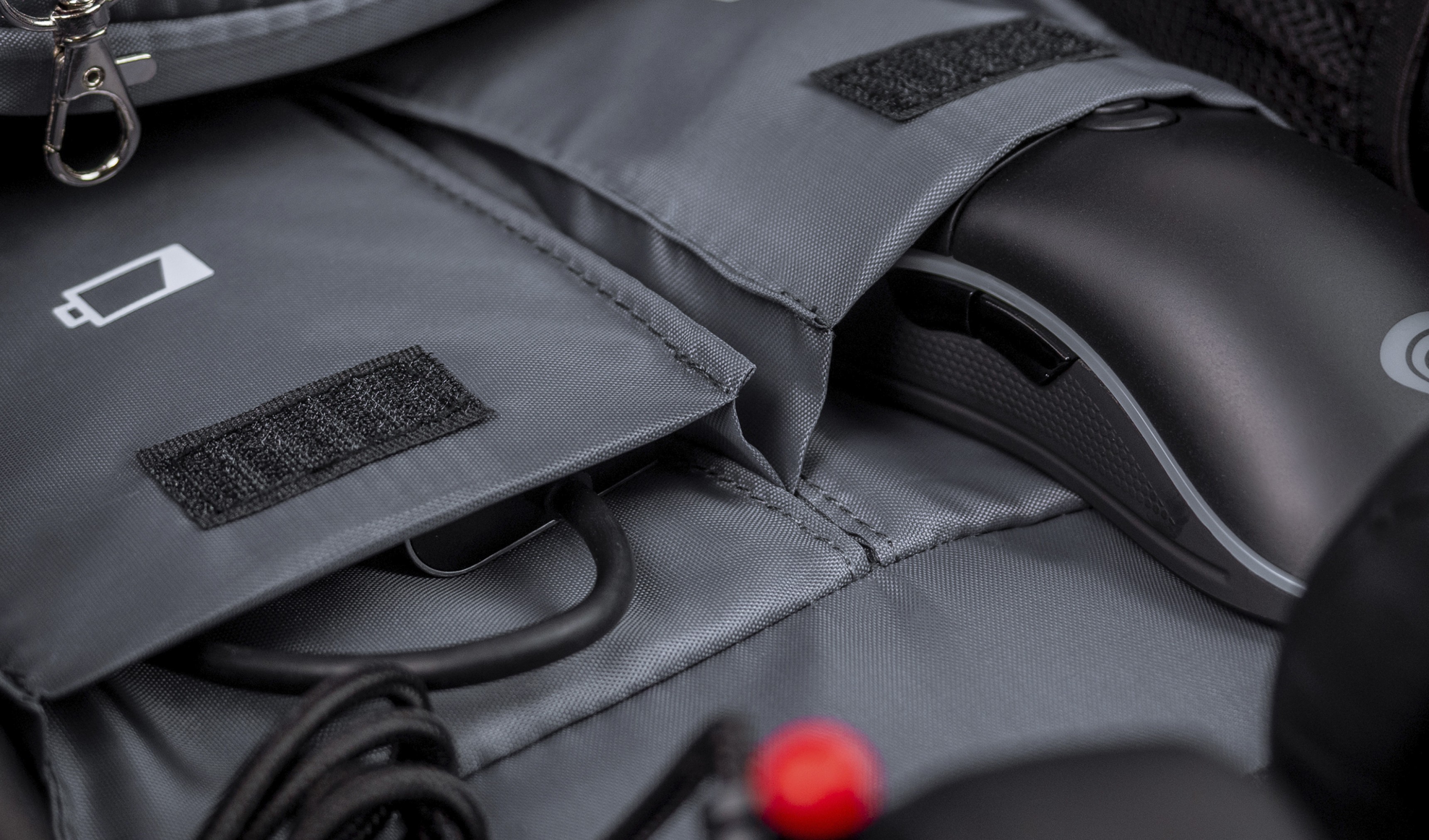 Interior gris de la mochila Genesis Pallad 550, mostrando compartimentos para un ratón y cables, con un icono de batería visible