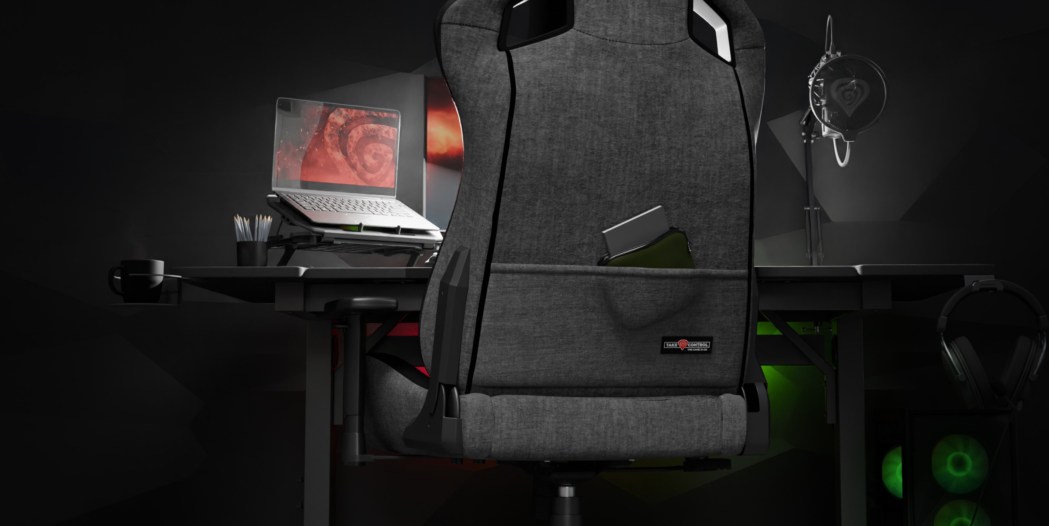 Silla de juego Genesis Nitro 660 gris colocada detrás de un escritorio con un portátil y accesorios de juego en una habitación poco iluminada