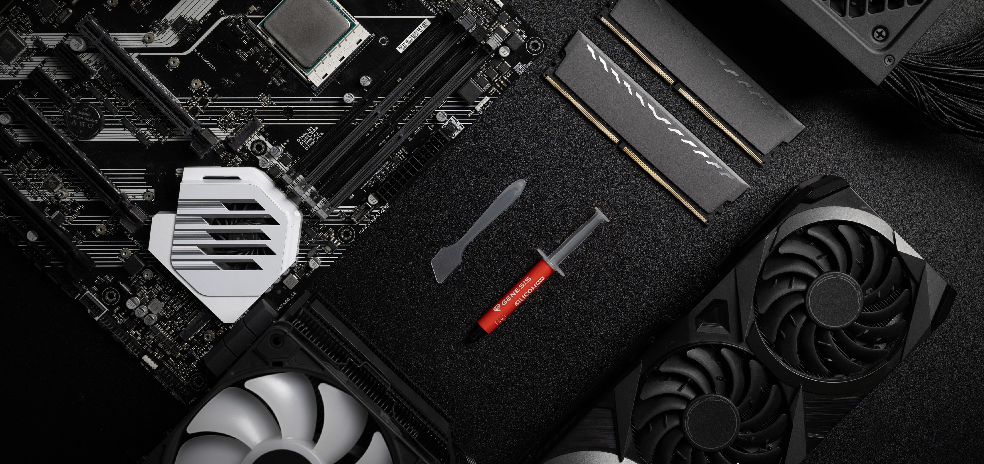 Tubo de pasta térmica con una espátula, colocado sobre un fondo negro junto a una placa base, RAM y GPU