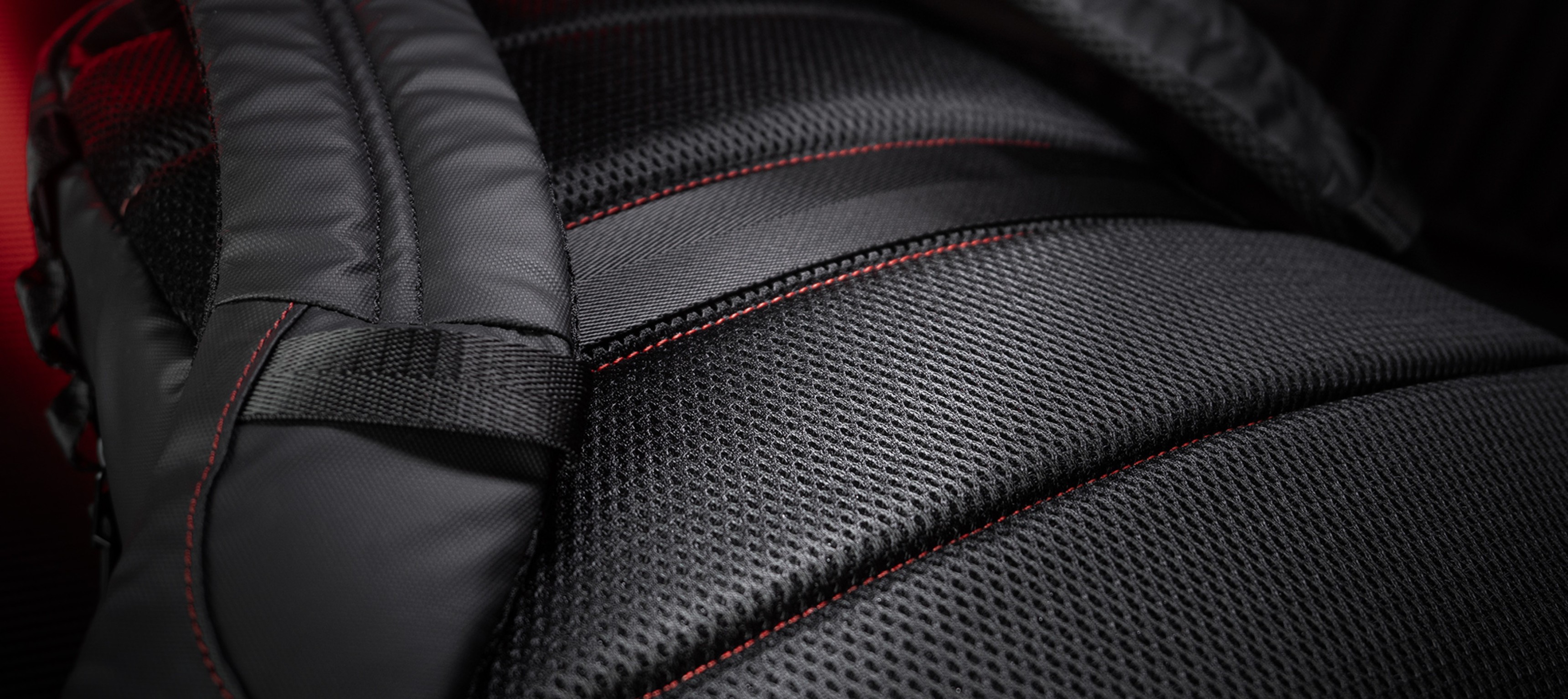 Primer plano de la mochila Genesis Pallad 420, mostrando su tejido negro texturizado con costuras rojas y correas acolchadas