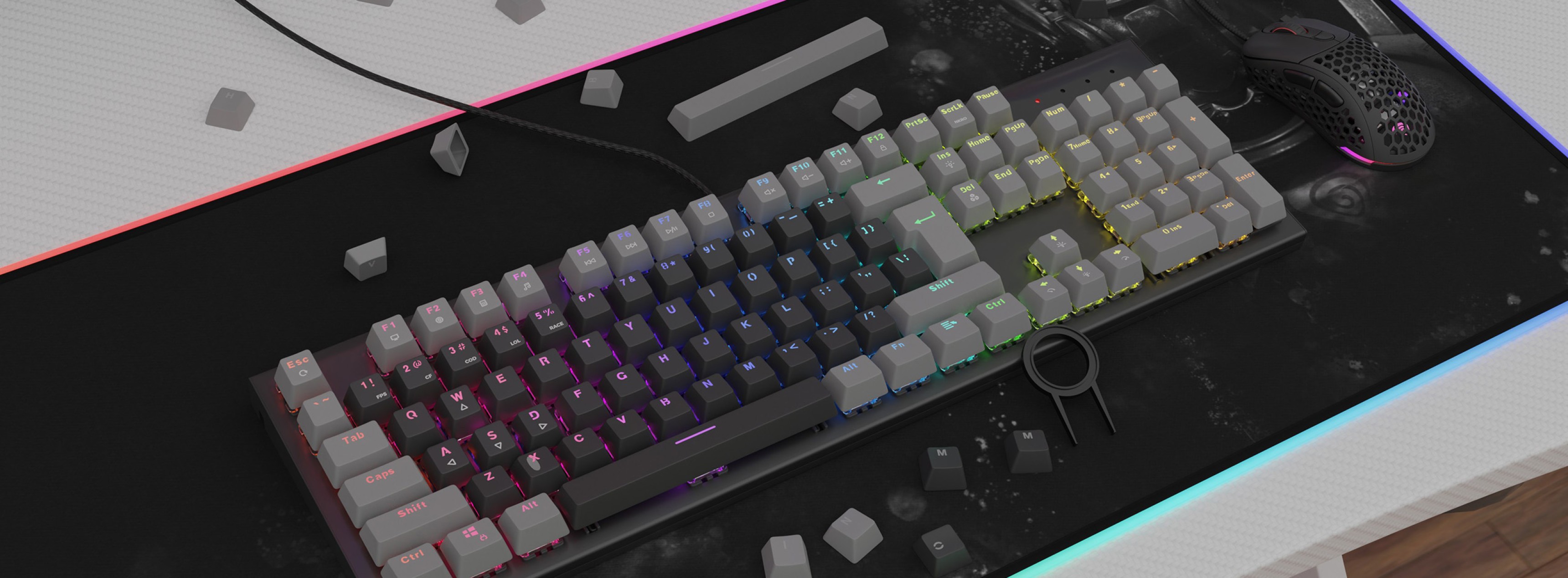 Un teclado mecánico con iluminación RGB de colores y teclas grises de doble disparo, colocado sobre una alfombrilla de ratón texturizada