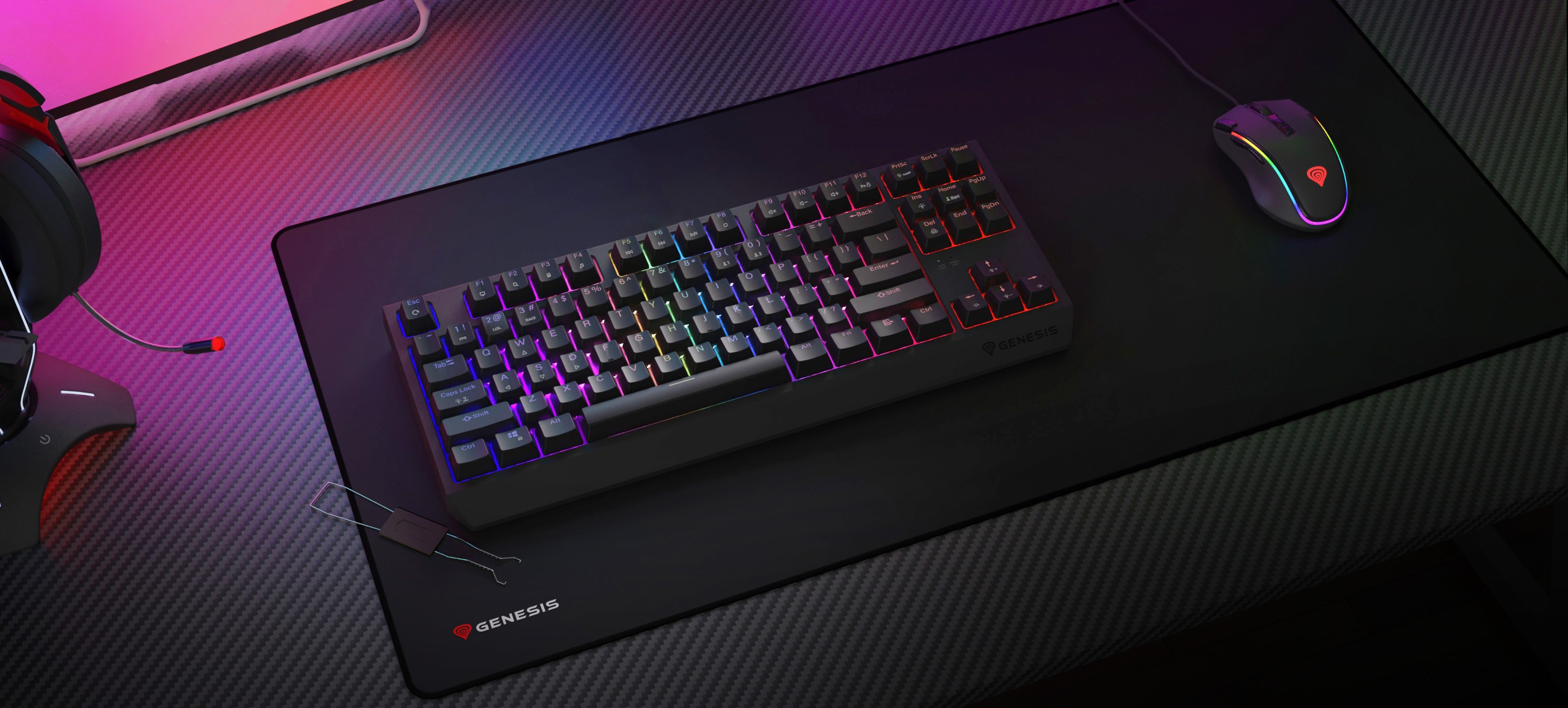 Teclado mecánico inalámbrico para juegos con iluminación RGB, colocado sobre una gran alfombrilla junto a un ratón para juegos y unos auriculares