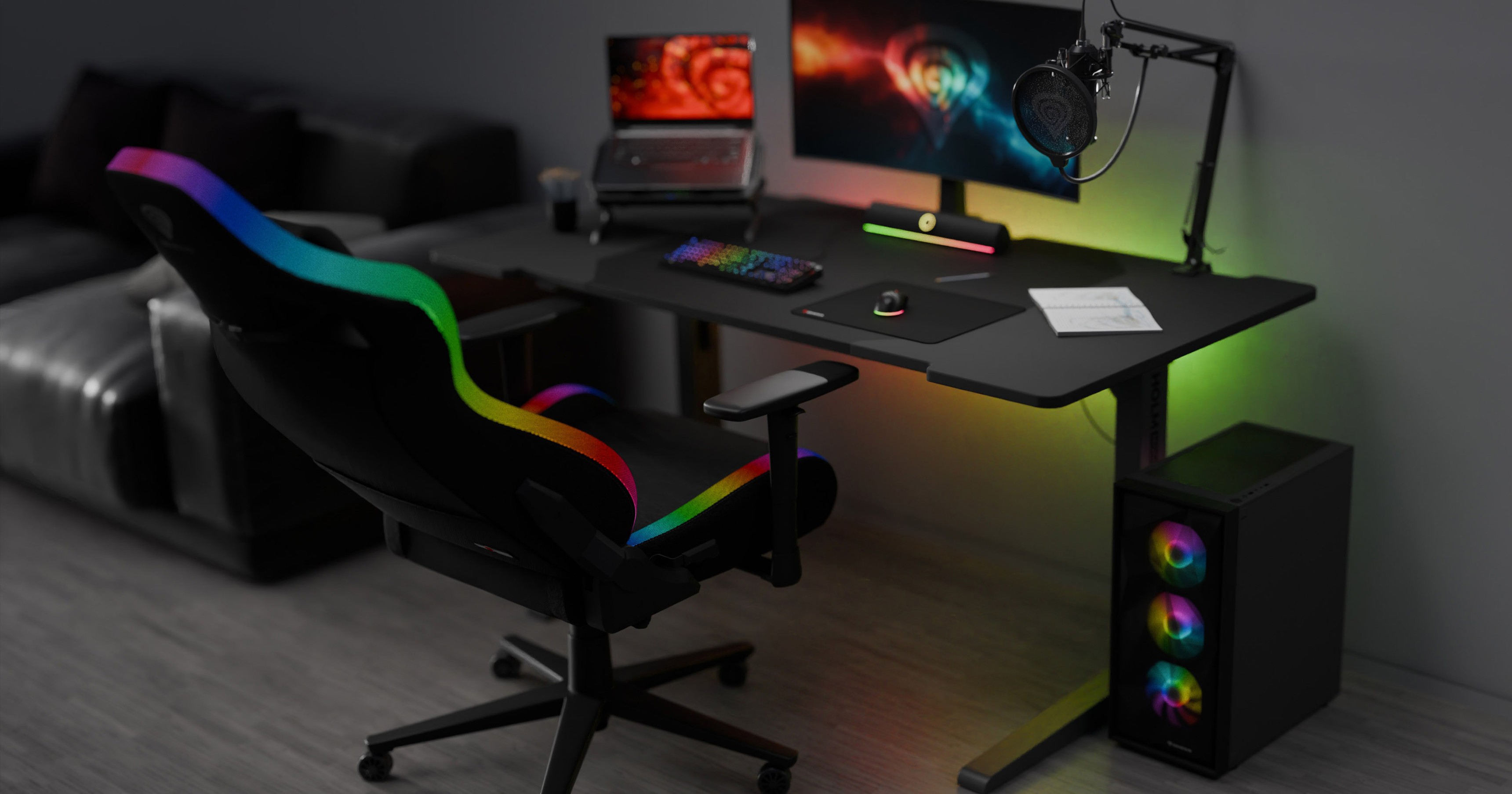 Una silla de juego negra con detalles RGB se sitúa junto a un elegante escritorio con un monitor, un teclado y una colorida configuración de juego
