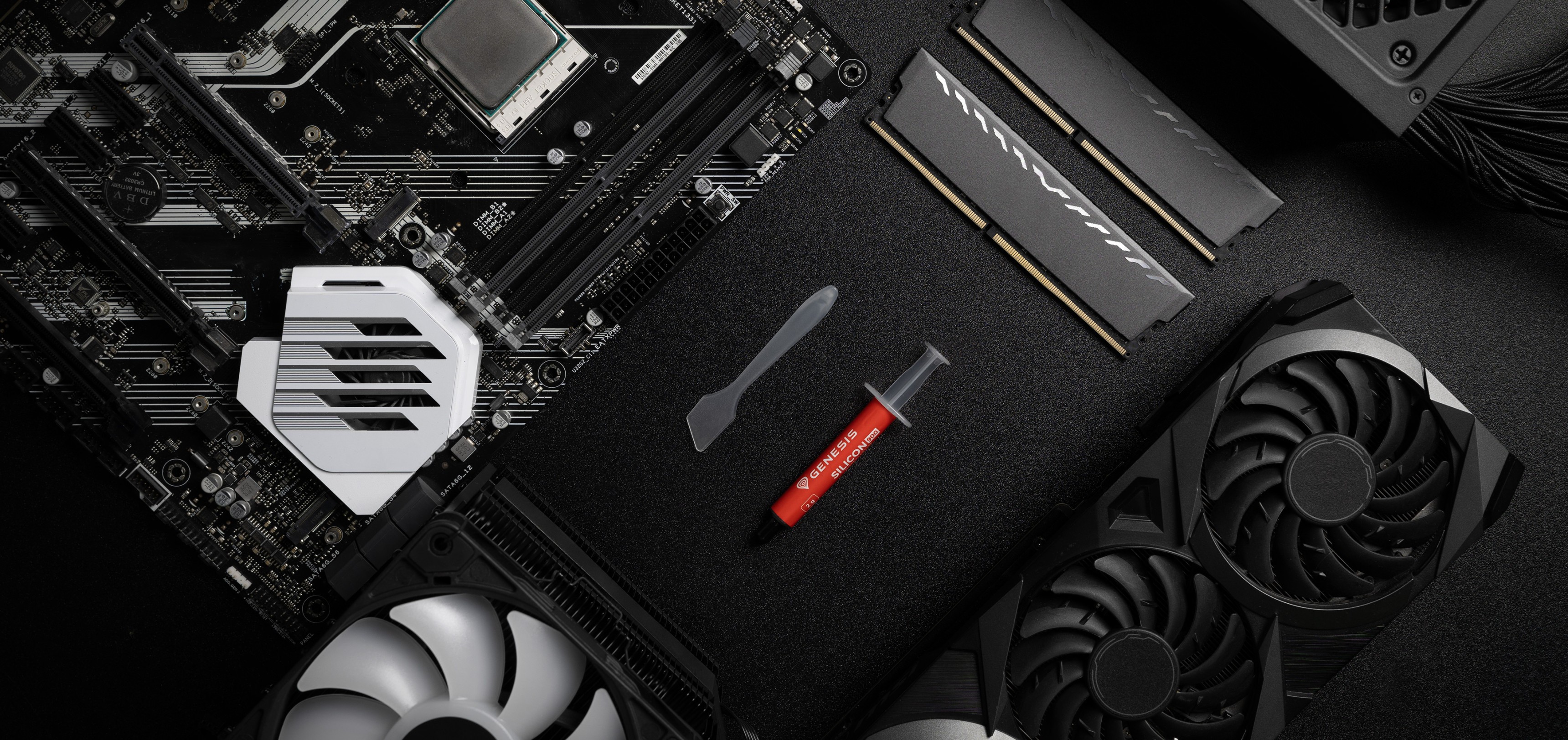 Tubo de pasta térmica con una espátula expuesto en una placa base, junto a componentes de RAM y GPU